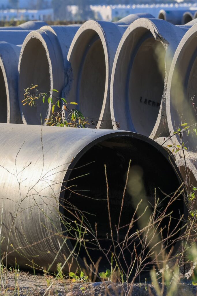 Stacked concrete pipes in an outdoor storage area surrounded by grass.