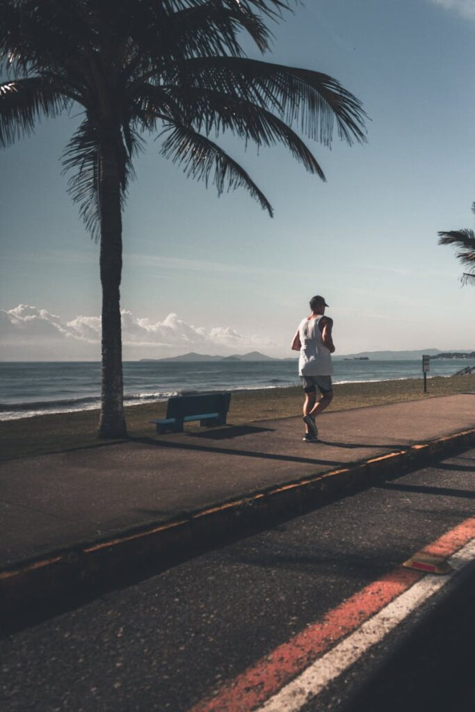 A man runs along a palm-lined seaside path, capturing the essence of morning fitness by the beach.