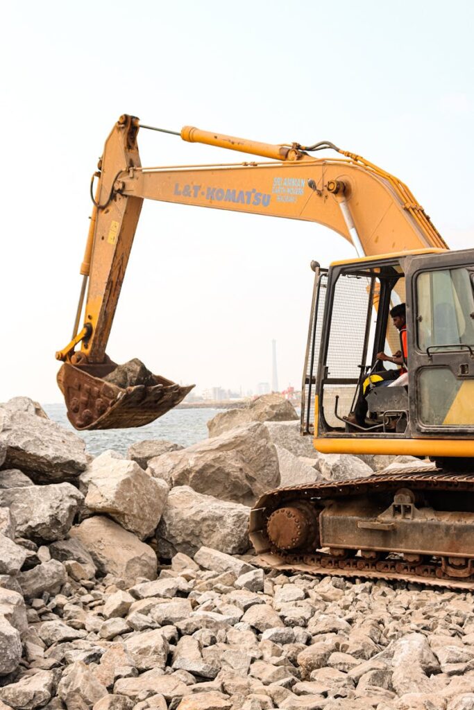 A large excavator moving rocks at an outdoor construction site near water.