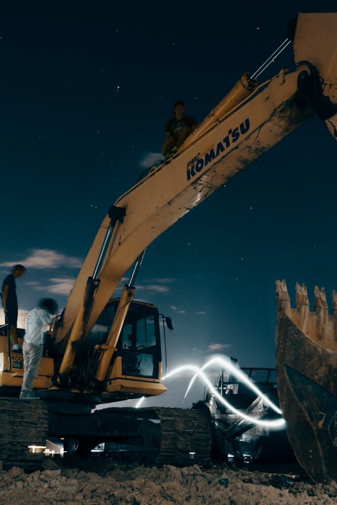 A powerful excavator at a construction site under the night sky, with workers around.