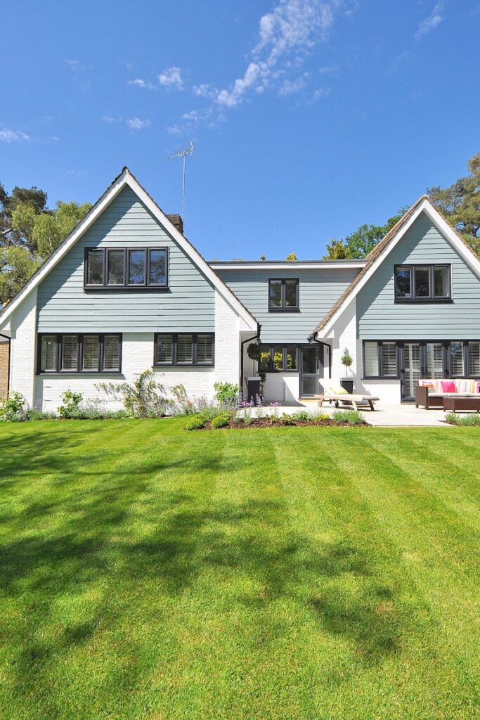 Modern family home exterior showcasing a large lawn and garden under a clear blue sky.