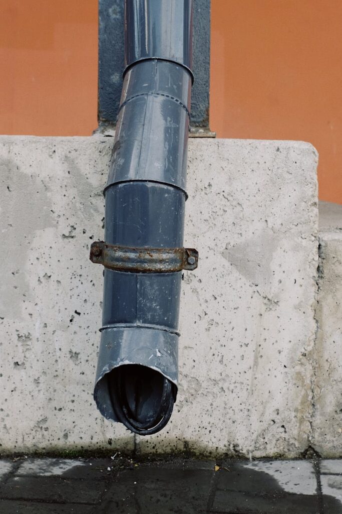 Aged metal drain pipe on a concrete wall with water stains, highlighting urban decay.