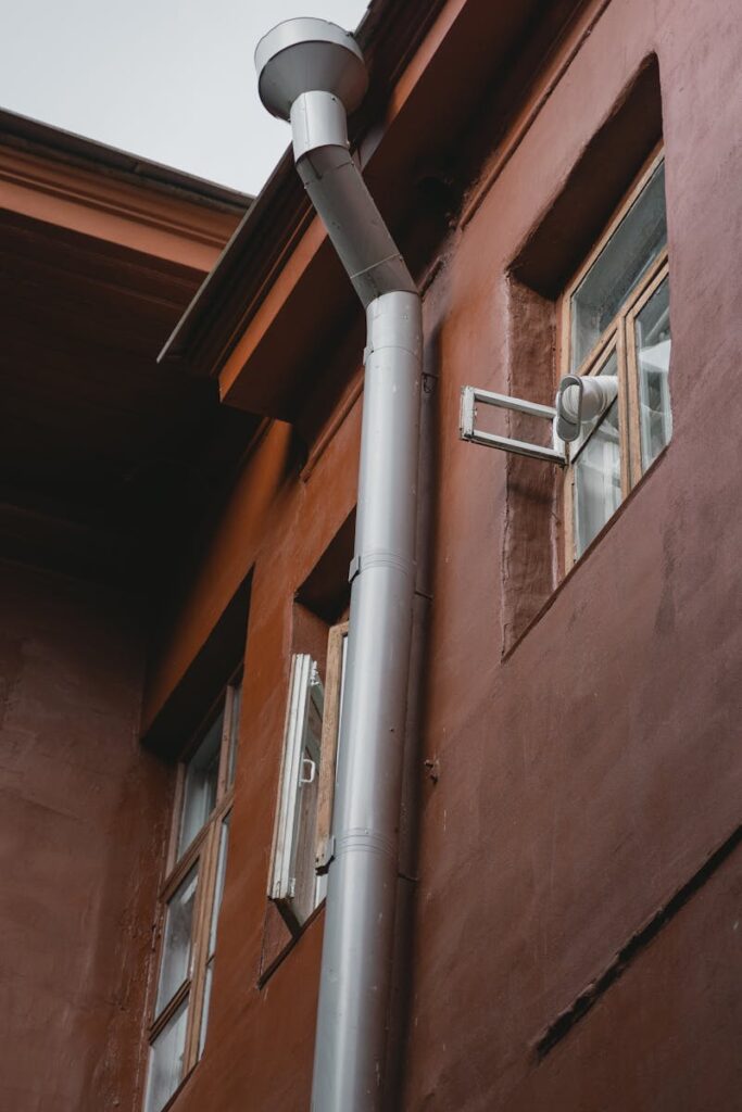 A brown building exterior with pipes and windows, photographed from a low angle.