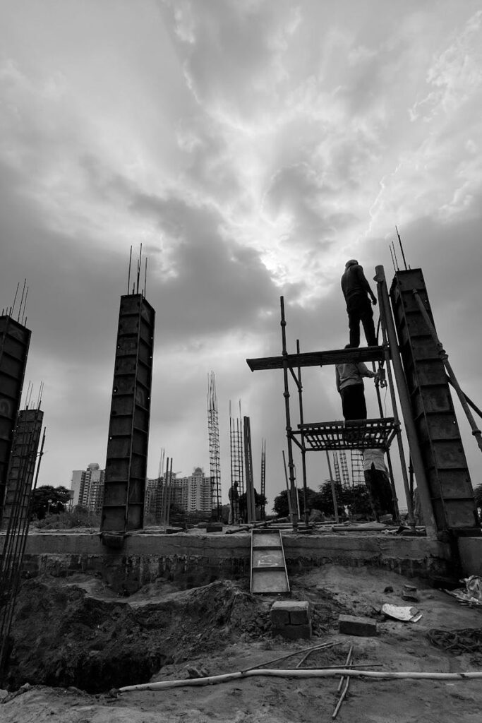 Black and white image capturing construction workers at a building site in Rasulpur, India.