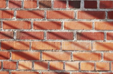 Red brick wall with striking shadows creating a textured pattern.