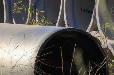 Stacked concrete pipes in an outdoor storage area surrounded by grass.