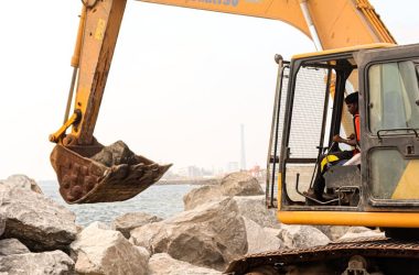 A large excavator moving rocks at an outdoor construction site near water.