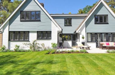 Modern family home exterior showcasing a large lawn and garden under a clear blue sky.